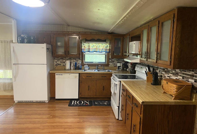 Kitchen featuring white appliances, vaulted ceiling, under cabinet range hood, light countertops, and tasteful backsplash