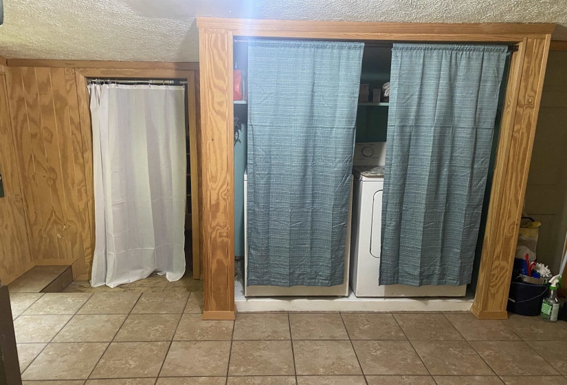 Bathroom featuring a textured ceiling, wood walls, washer / dryer, and tile patterned flooring