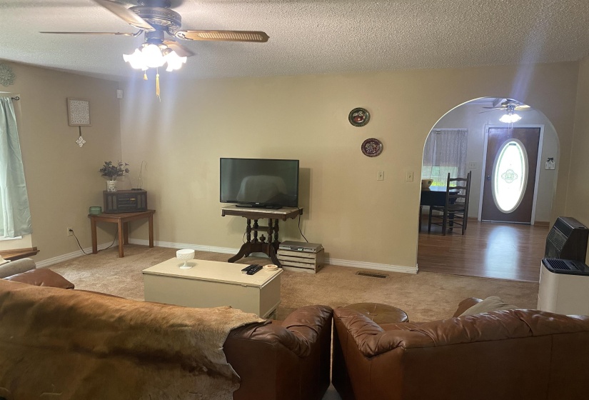 Living area with a ceiling fan, carpet floors, arched walkways, and a textured ceiling