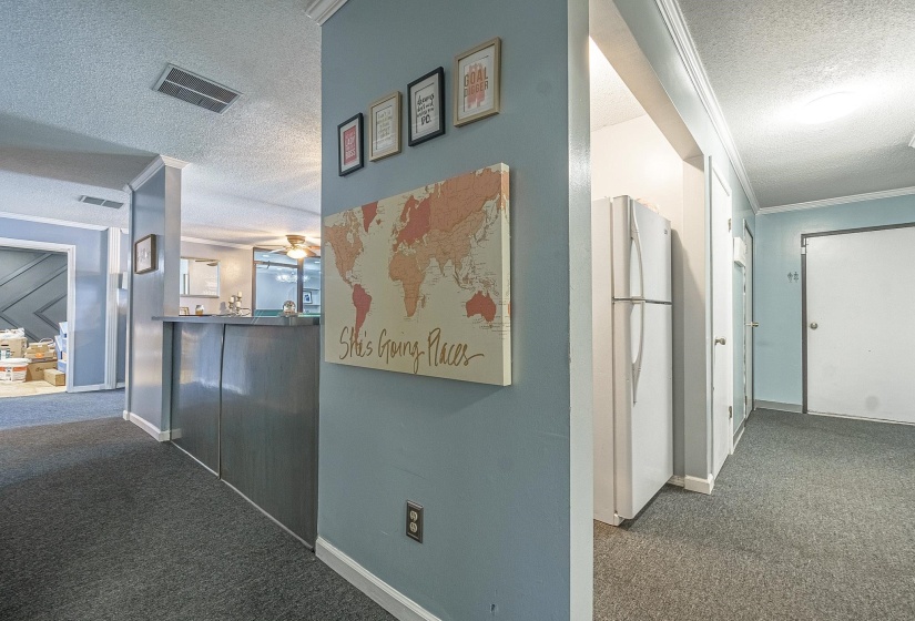 Hall featuring dark carpet, ornamental molding, and a textured ceiling