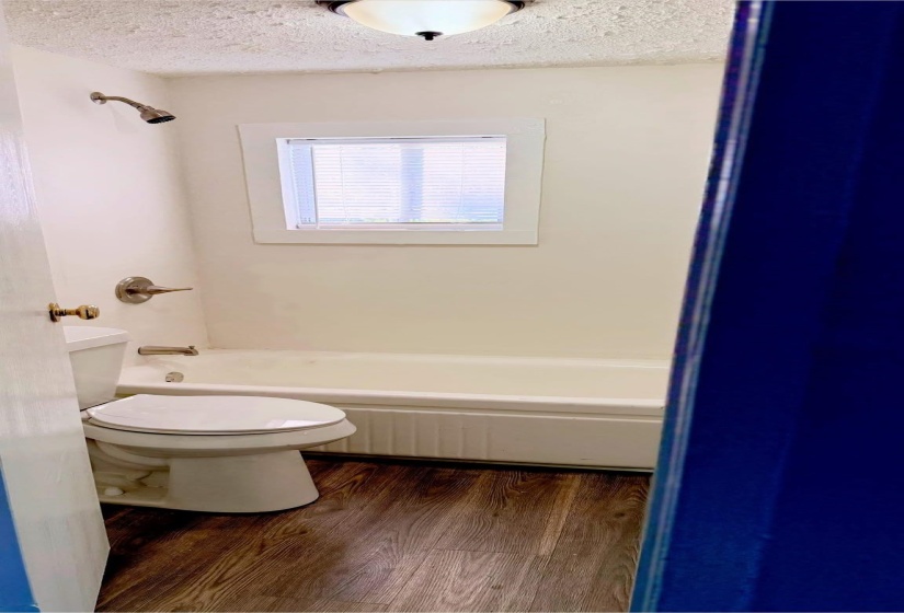Bathroom with tub / shower combination, wood-type flooring, a textured ceiling, and toilet