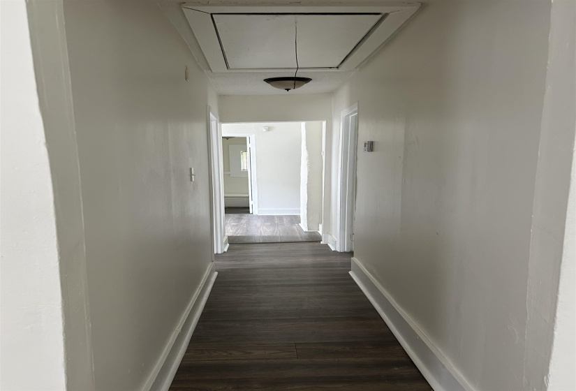 Corridor featuring attic access and dark wood-style flooring