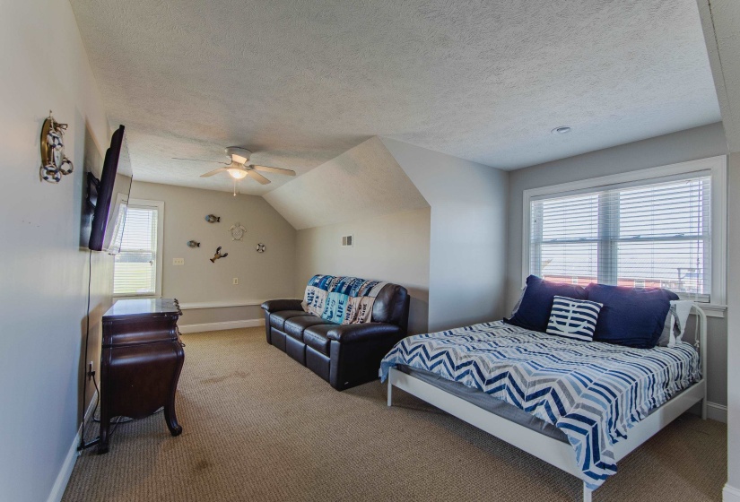 Carpeted bedroom with a textured ceiling, multiple windows, ceiling fan, and lofted ceiling