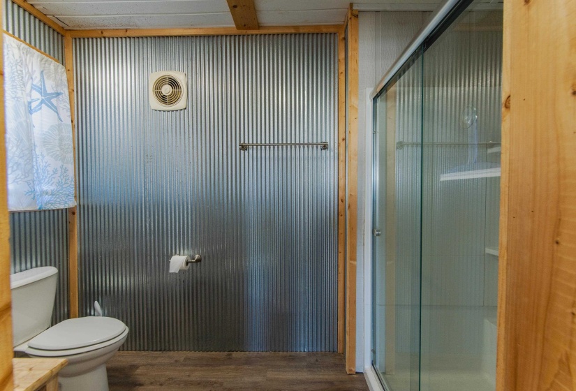 Bathroom with a shower with shower door, toilet, and wood-type flooring