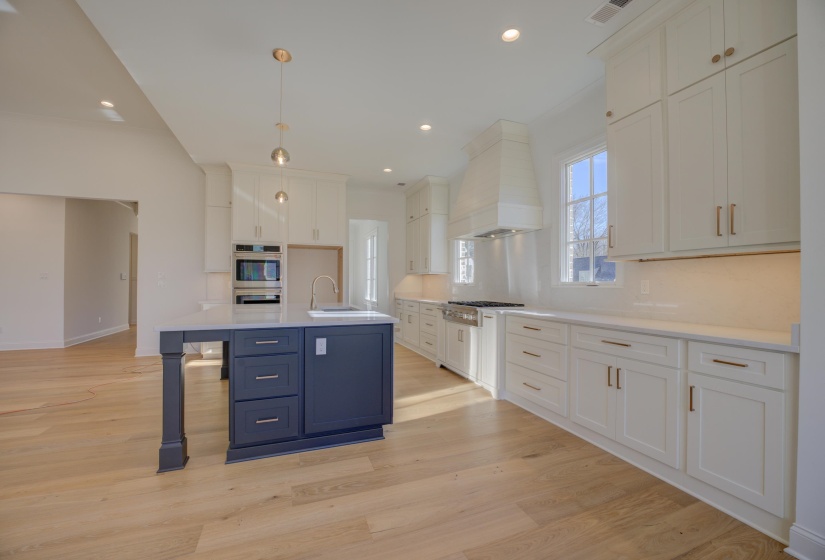 Kitchen featuring premium range hood, hanging light fixtures, light wood-type flooring, an island with sink, and white cabinetry