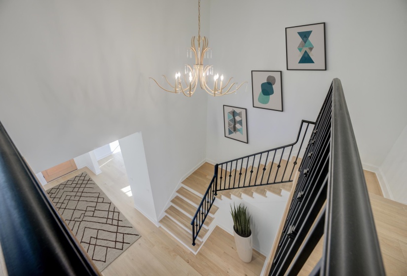 A grand staircase with polished hardwood floors and neutral walls, highlighted by a striking black stair rail. A statement chandelier hangs above, adding a touch of elegance and grandeur to the space.