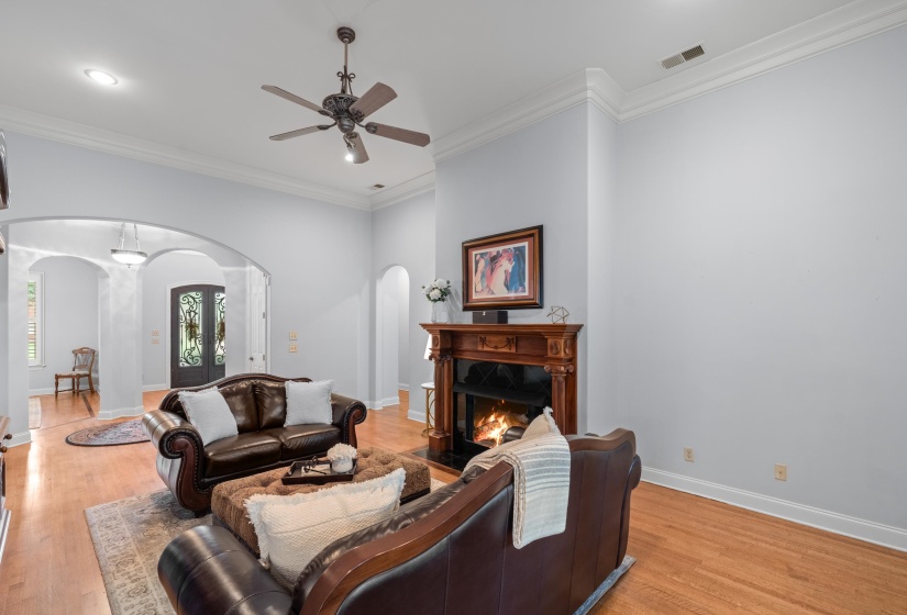 Living room with arched walkways, a ceiling fan, crown molding, light wood-type flooring, and a high end fireplace