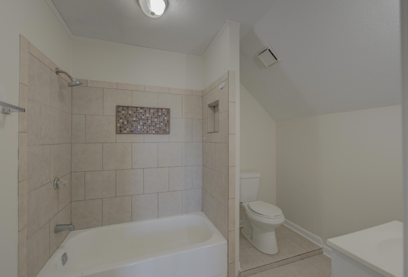 Full bathroom with vanity, tile patterned floors, tiled shower / bath, toilet, and a textured ceiling
