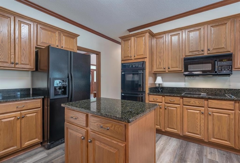 Kitchen with ornamental molding, a center island, black appliances, and wood-type flooring