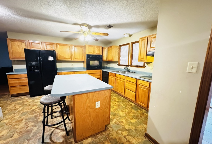 Kitchen with a center island, sink, a kitchen breakfast bar, a textured ceiling, and black appliances