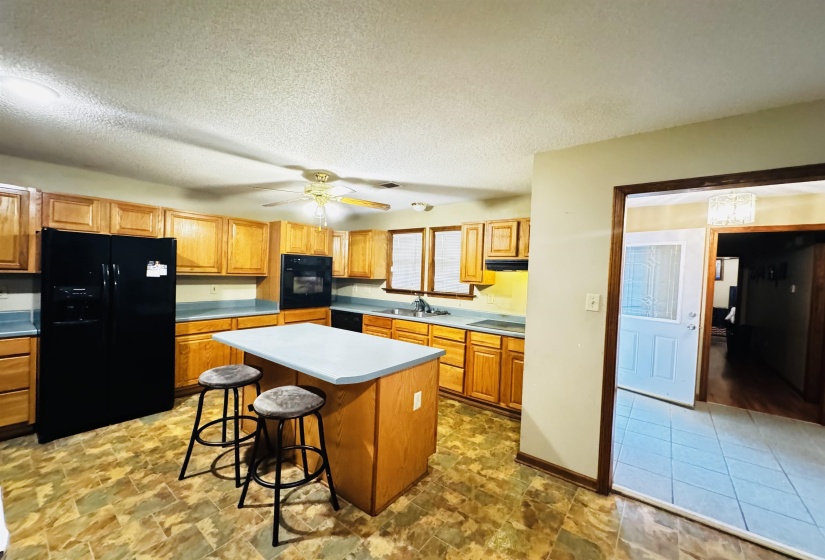 Kitchen featuring ceiling fan, a kitchen breakfast bar, a textured ceiling, a kitchen island, and black appliances