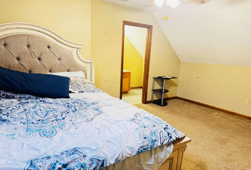 Carpeted bedroom with ceiling fan, lofted ceiling, and connected bathroom