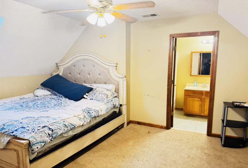 Bedroom featuring ensuite bath, light colored carpet, ceiling fan, sink, and lofted ceiling