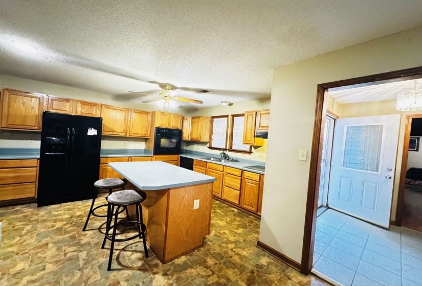 Kitchen with a kitchen bar, a textured ceiling, sink, black appliances, and a kitchen island