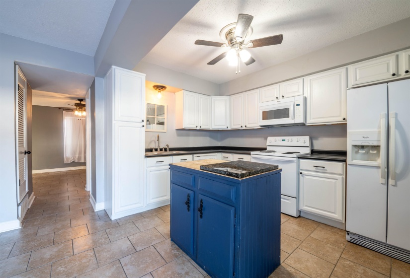 Kitchen with white appliances, white cabinets, sink, ceiling fan, and a kitchen island