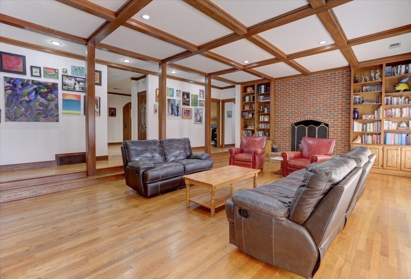 Living area with light wood-style floors, a brick fireplace, built in features, visible vents, and coffered ceiling