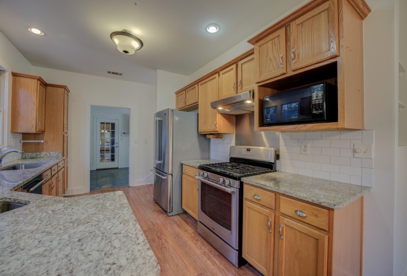 Kitchen featuring sink, light hardwood / wood-style flooring, light stone countertops, appliances with stainless steel finishes, and tasteful backsplash
