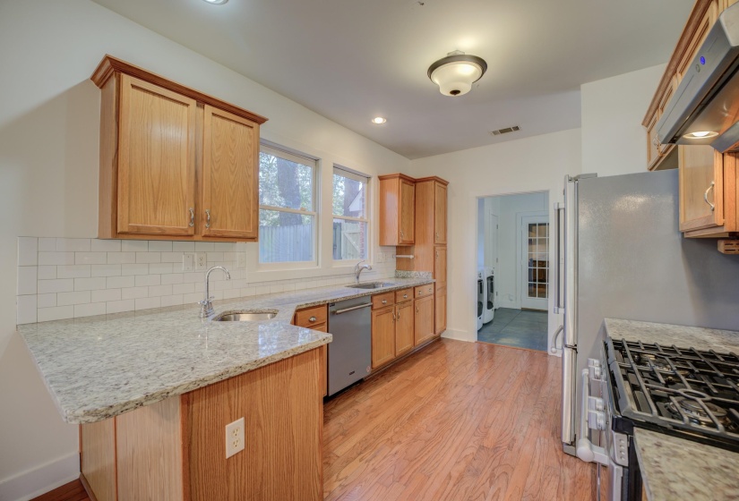 Kitchen with exhaust hood, sink, light stone countertops, kitchen peninsula, and stainless steel appliances
