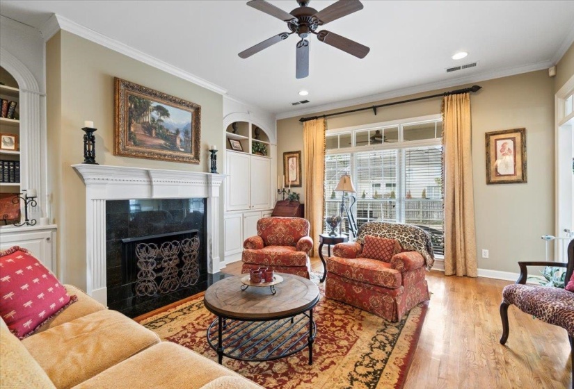 Living room with a high end fireplace, light hardwood / wood-style floors, built in features, ceiling fan, and crown molding