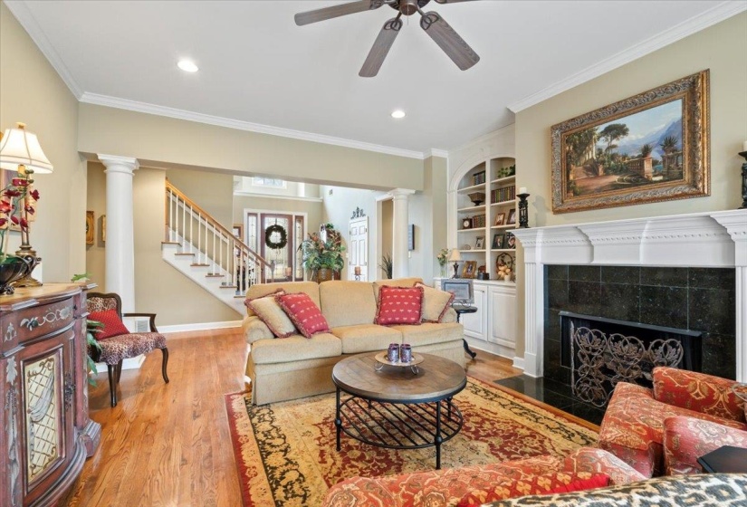 Living room featuring built in shelves, a fireplace, ceiling fan, light hardwood / wood-style flooring, and crown molding