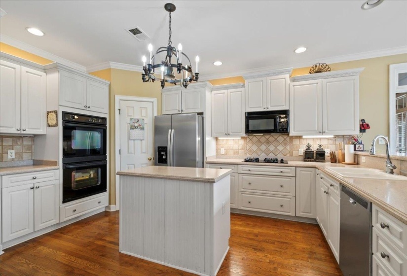 Kitchen featuring dark hardwood / wood-style floors, black appliances, sink, an inviting chandelier, and white cabinetry