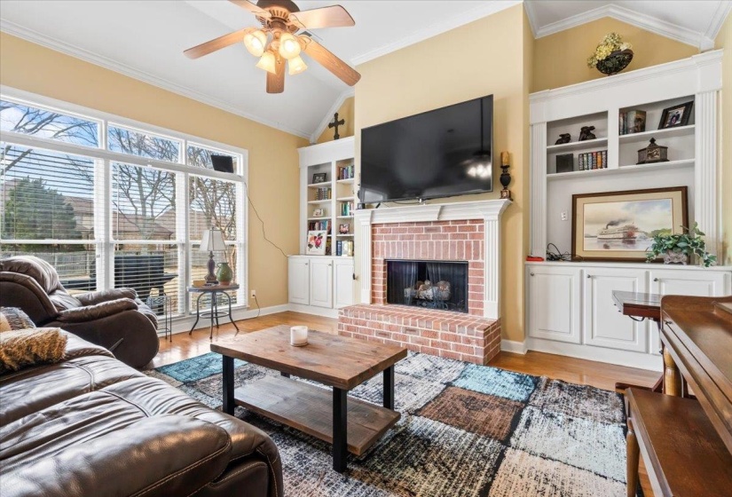 Living room with ceiling fan, a fireplace, wood-type flooring, vaulted ceiling, and ornamental molding