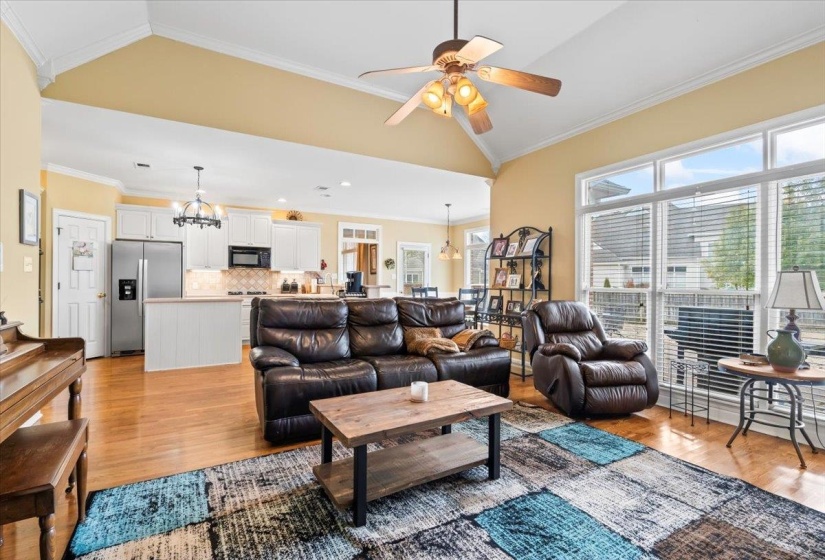 Living room with ceiling fan with notable chandelier, lofted ceiling, and ornamental molding