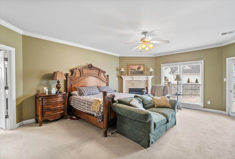 Carpeted bedroom featuring ceiling fan, a fireplace, and crown molding