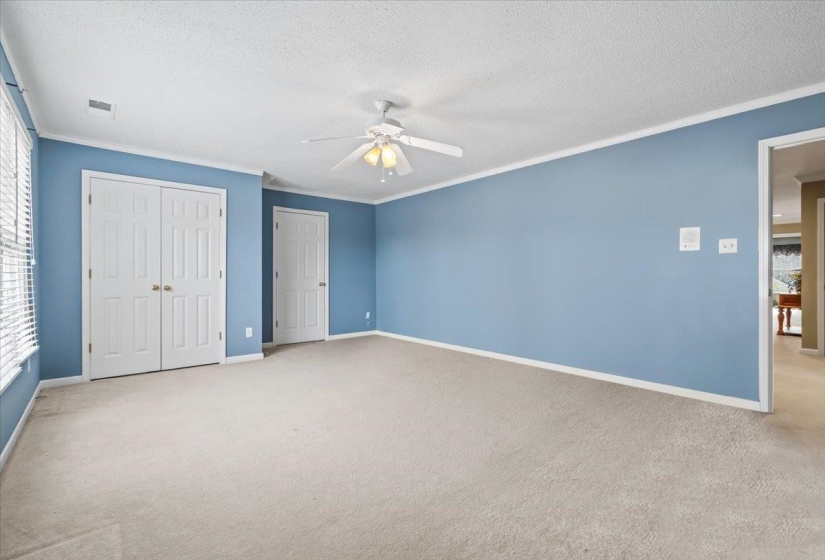 Unfurnished bedroom with ceiling fan, light colored carpet, and ornamental molding