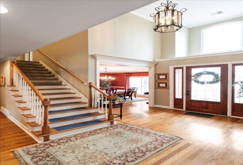 Entrance foyer with wood-type flooring, a notable chandelier, a towering ceiling, and ornamental molding