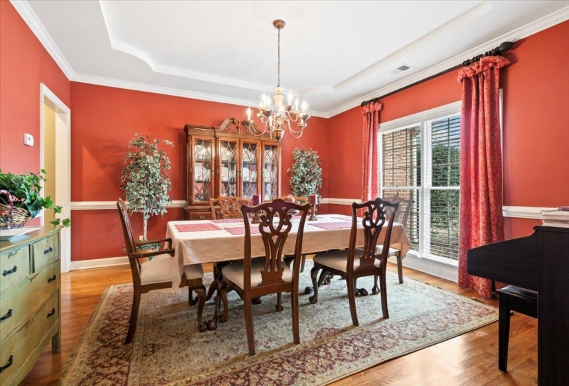 Dining area with an inviting chandelier, a tray ceiling, ornamental molding, and hardwood / wood-style flooring