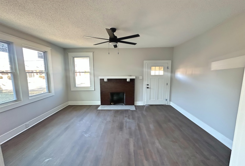 Unfurnished living room with ceiling fan, a brick fireplace, a textured ceiling, and dark hardwood / wood-style floors