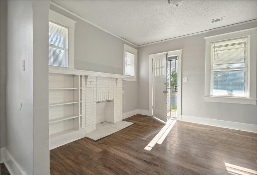 Unfurnished living room featuring a brick fireplace, dark wood-type flooring, a textured ceiling, and a healthy amount of sunlight