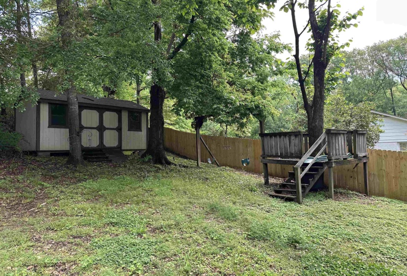 Fenced backyard featuring a shed, an outdoor structure, and a deck