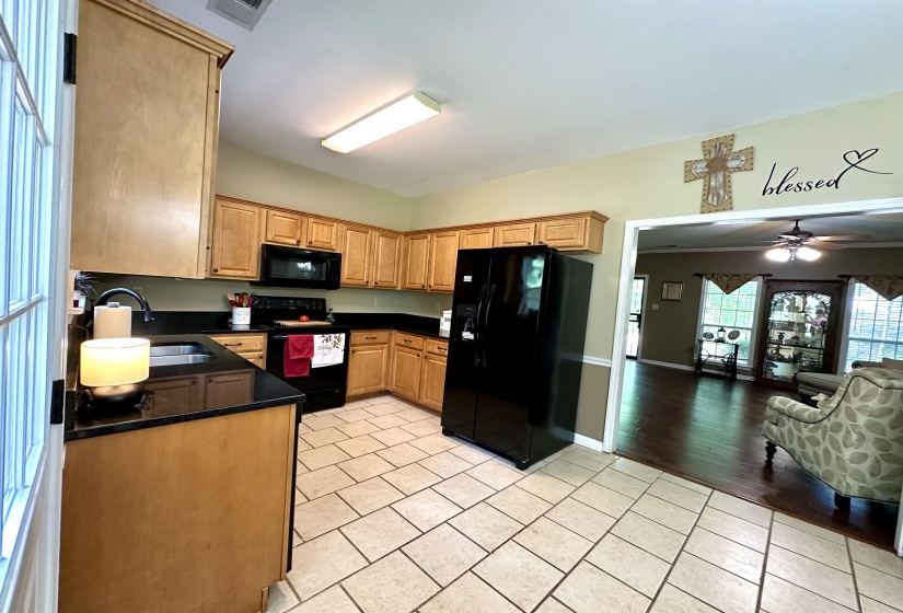 Kitchen featuring black appliances, a sink, light tile patterned floors, dark countertops, and light brown cabinetry