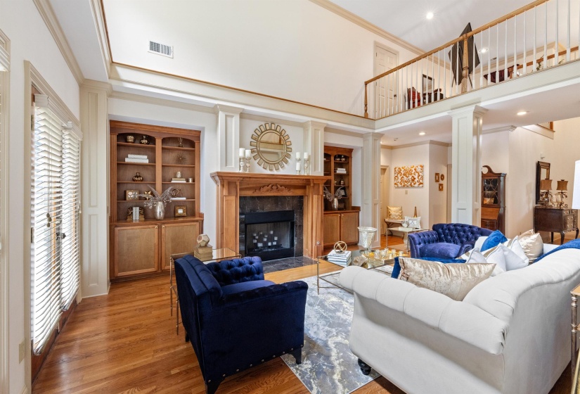 Living room featuring a towering ceiling, wood-type flooring, decorative columns, a fireplace, and crown molding
