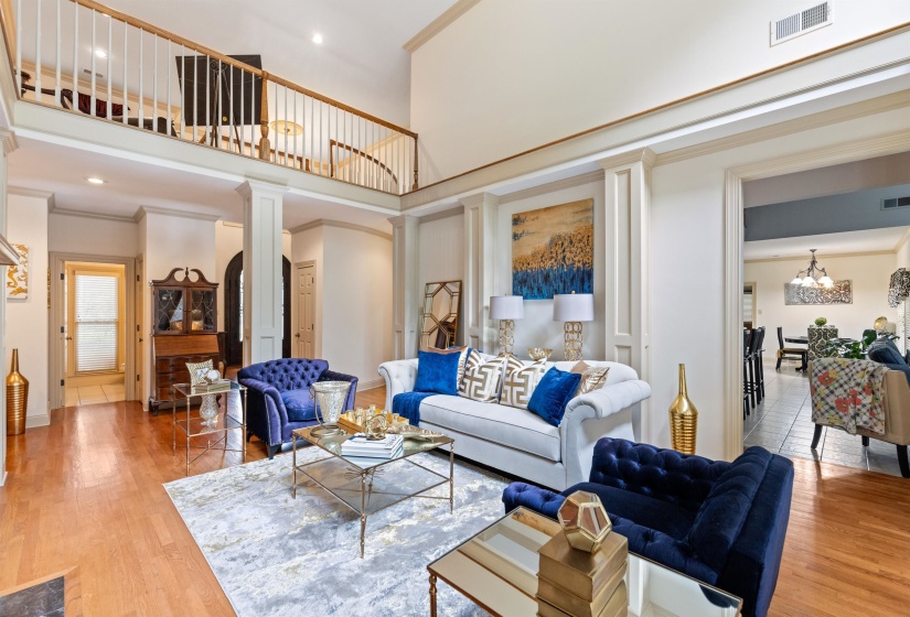 Living room featuring wood-type flooring, decorative columns, a high ceiling, a notable chandelier, and crown molding