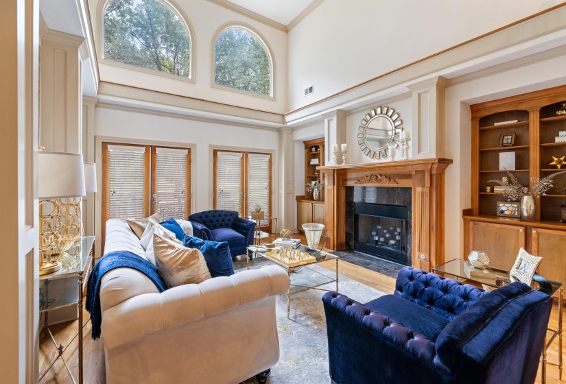 Living room with light hardwood / wood-style flooring, a towering ceiling, ornamental molding, and a high end fireplace