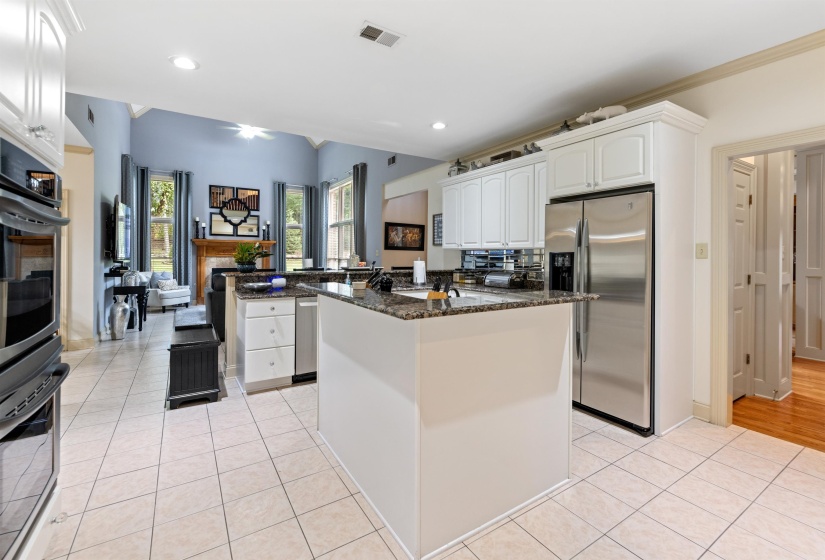 Kitchen with dark stone counters, stainless steel fridge, light tile patterned floors, and white cabinets