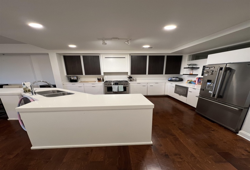 Kitchen with dark wood-type flooring, sink, a center island with sink, stainless steel appliances, and white cabinets