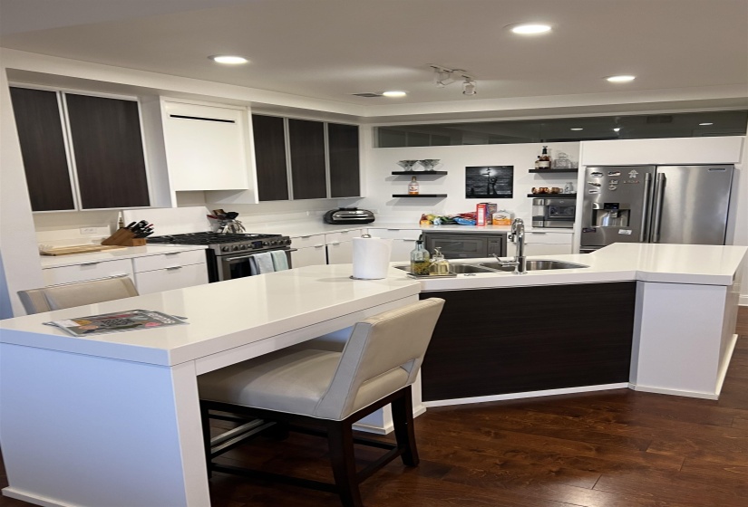 Kitchen featuring sink, a center island with sink, high end appliances, a kitchen bar, and dark hardwood / wood-style flooring