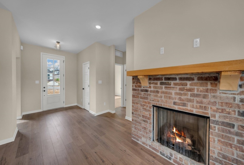 Unfurnished living room featuring wood-type flooring, a brick fireplace, and baseboards