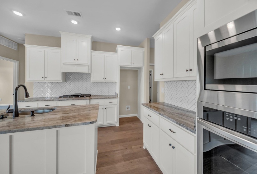 Kitchen with white cabinets, wood finished floors, light stone countertops, and a sink
