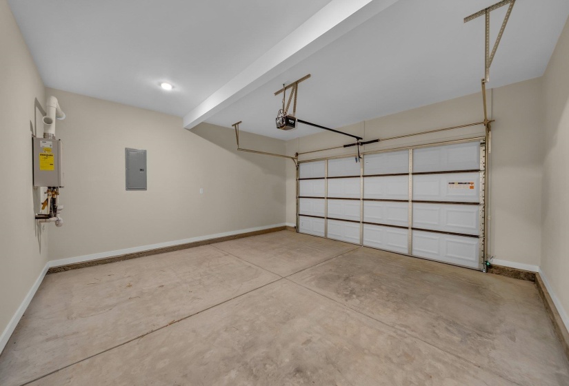 Garage with electric panel, a garage door opener, baseboards, and water heater