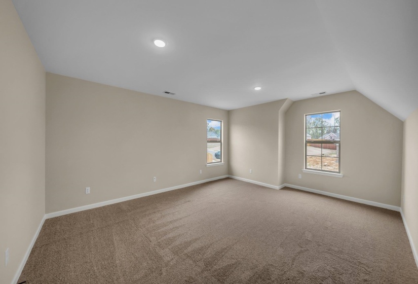 Carpeted empty room featuring baseboards, visible vents, lofted ceiling, and a healthy amount of sunlight