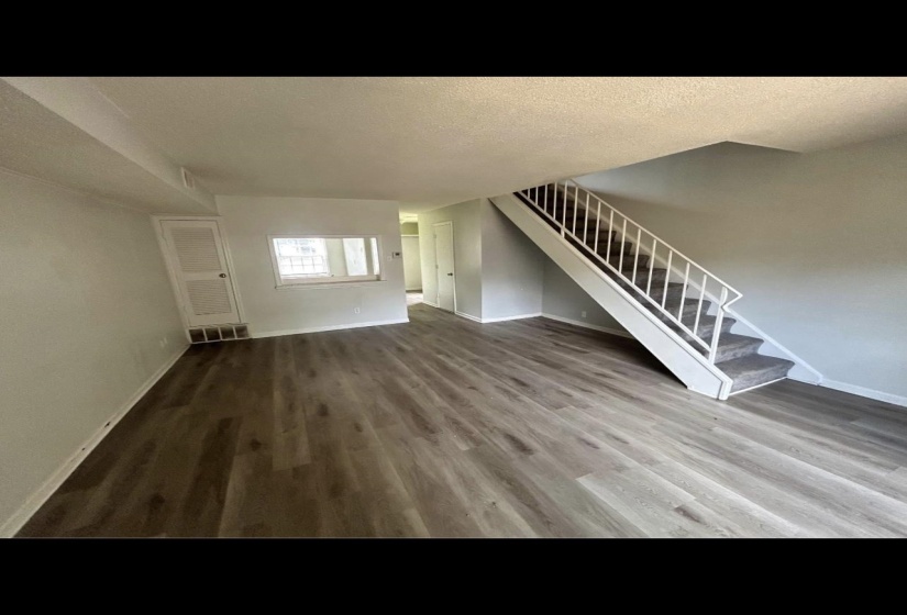 Unfurnished living room featuring visible vents, baseboards, wood finished floors, stairs, and a textured ceiling