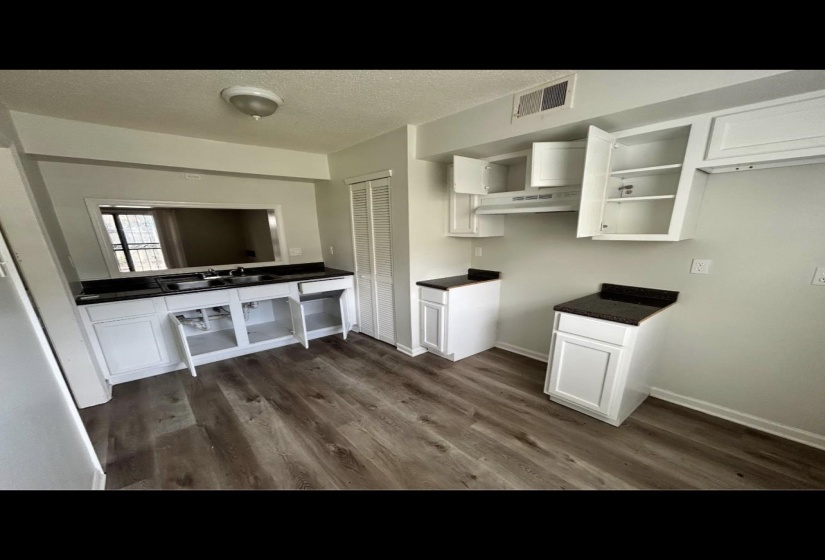 Interior space featuring dark countertops, under cabinet range hood, white cabinetry, and dark wood-style floors