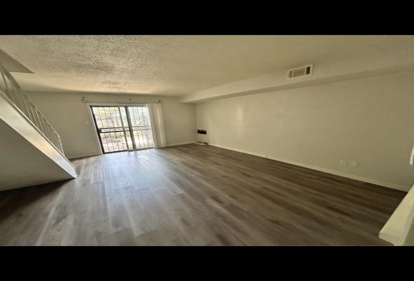 Unfurnished living room with a textured ceiling, wood finished floors, visible vents, baseboards, and stairway