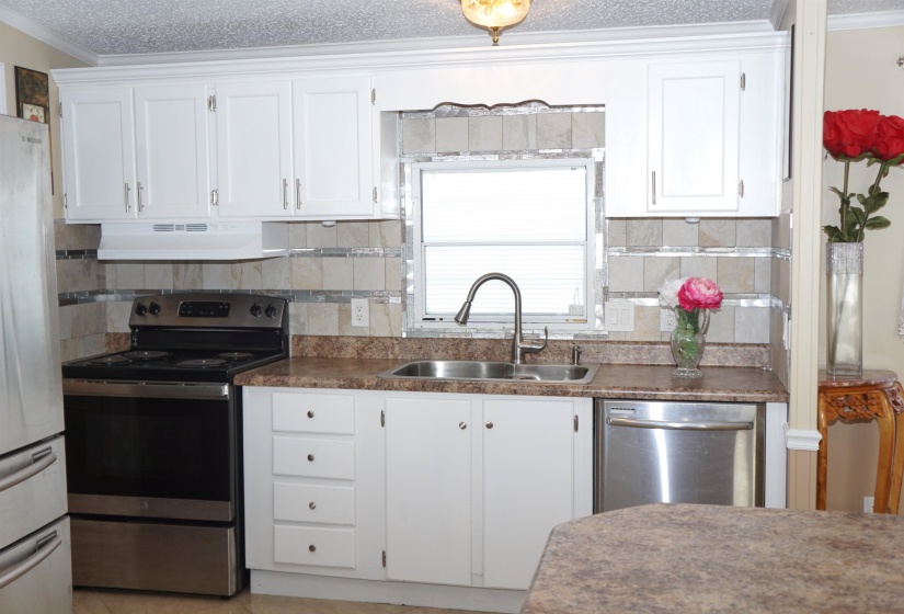 Kitchen featuring under cabinet range hood, a sink, white cabinets, appliances with stainless steel finishes, and crown molding