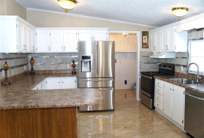 Kitchen with crown molding, stainless steel appliances, vaulted ceiling, a sink, and under cabinet range hood